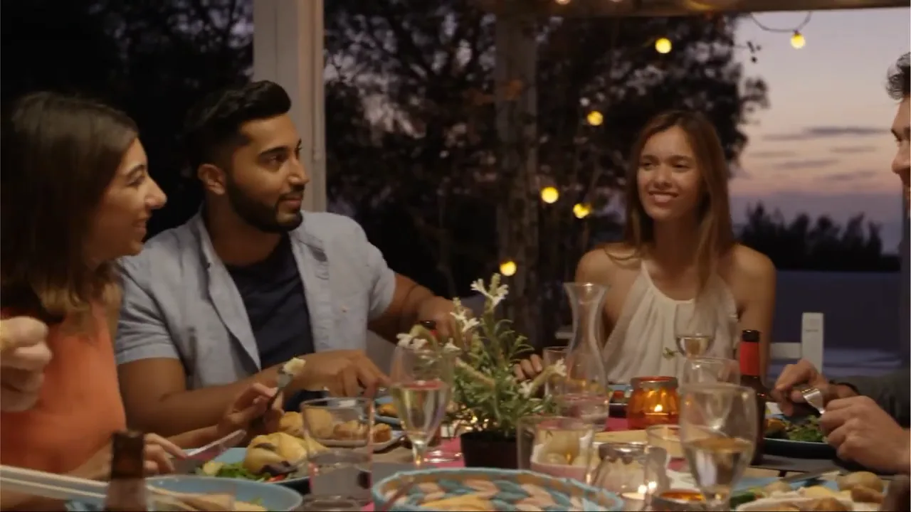 A frame from the spot: friends around a string-lit dusk dinner table, shot as live footage rather than animated type.